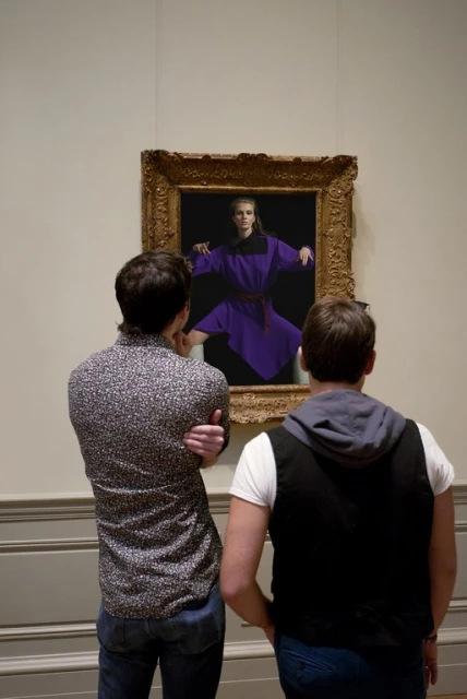Two men view an art gallery painting of a woman in purple, standing in front of a dark background, in an ornate gold frame.