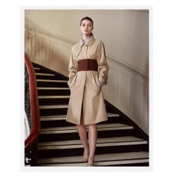 Model standing on a staircase wearing a beige trench coat with a wide brown waist belt photographed by Cesar Love Alexandre
