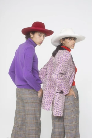 Two models wearing wide-brimmed hats and colorful patterned autumn clothing against a plain white studio background.