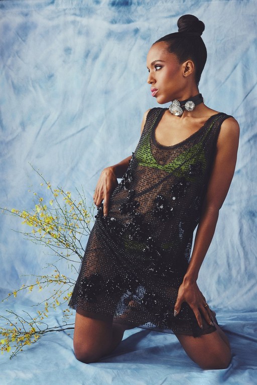 Black woman in semi-sheer black mini dress poses against a light blue backdrop with yellow floral sprigs. Fashion shot, full studio lighting.