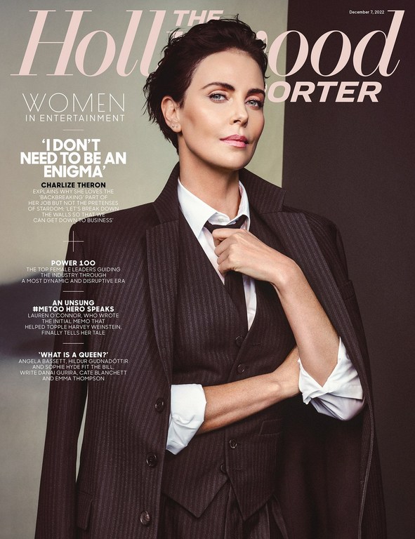 Charlize Theron on the cover of The Hollywood Reporter wearing a suit, tie, and coat in a portrait shot with a two-tone background.