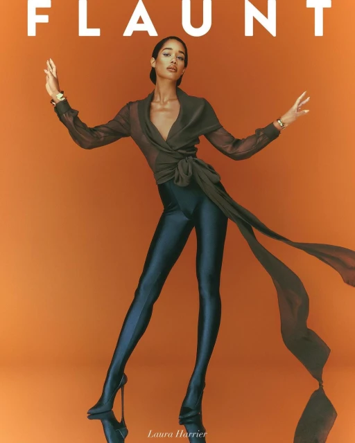 Elegant woman poses in translucent wrap top, shiny leggings, and high heels against a warm orange background for a fashion editorial.