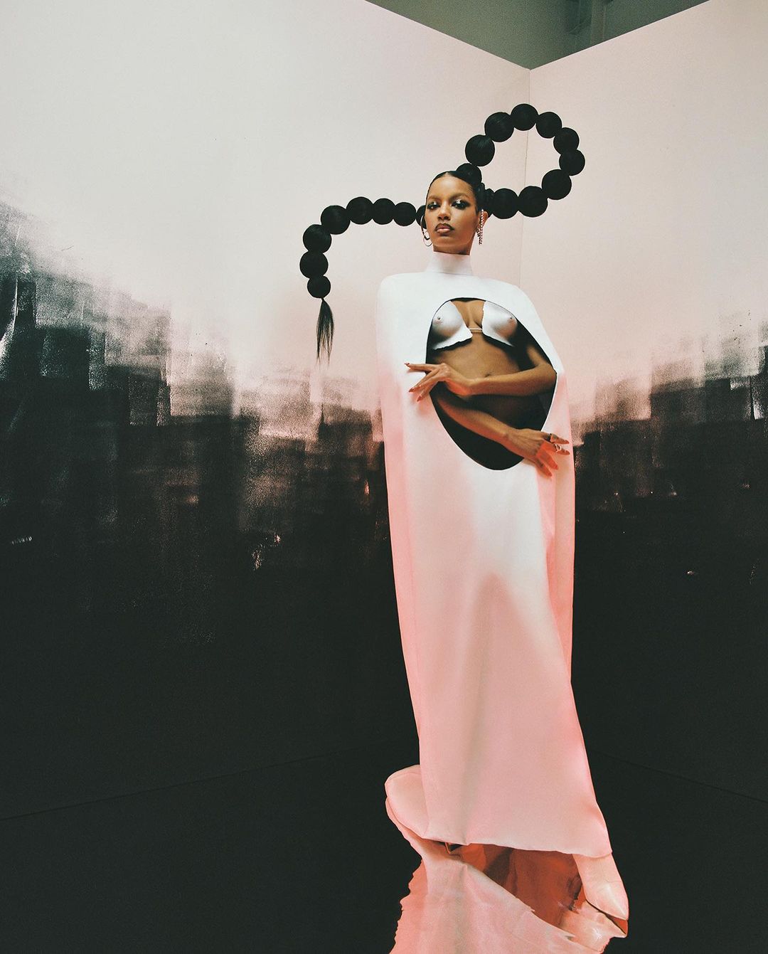 Woman in avant-garde fashion with unique hairstyle, posing in a studio against a backdrop of contrasting light and dark paint.