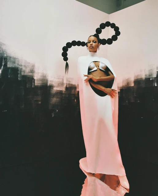 Woman in avant-garde fashion with unique hairstyle, posing in a studio against a backdrop of contrasting light and dark paint.
