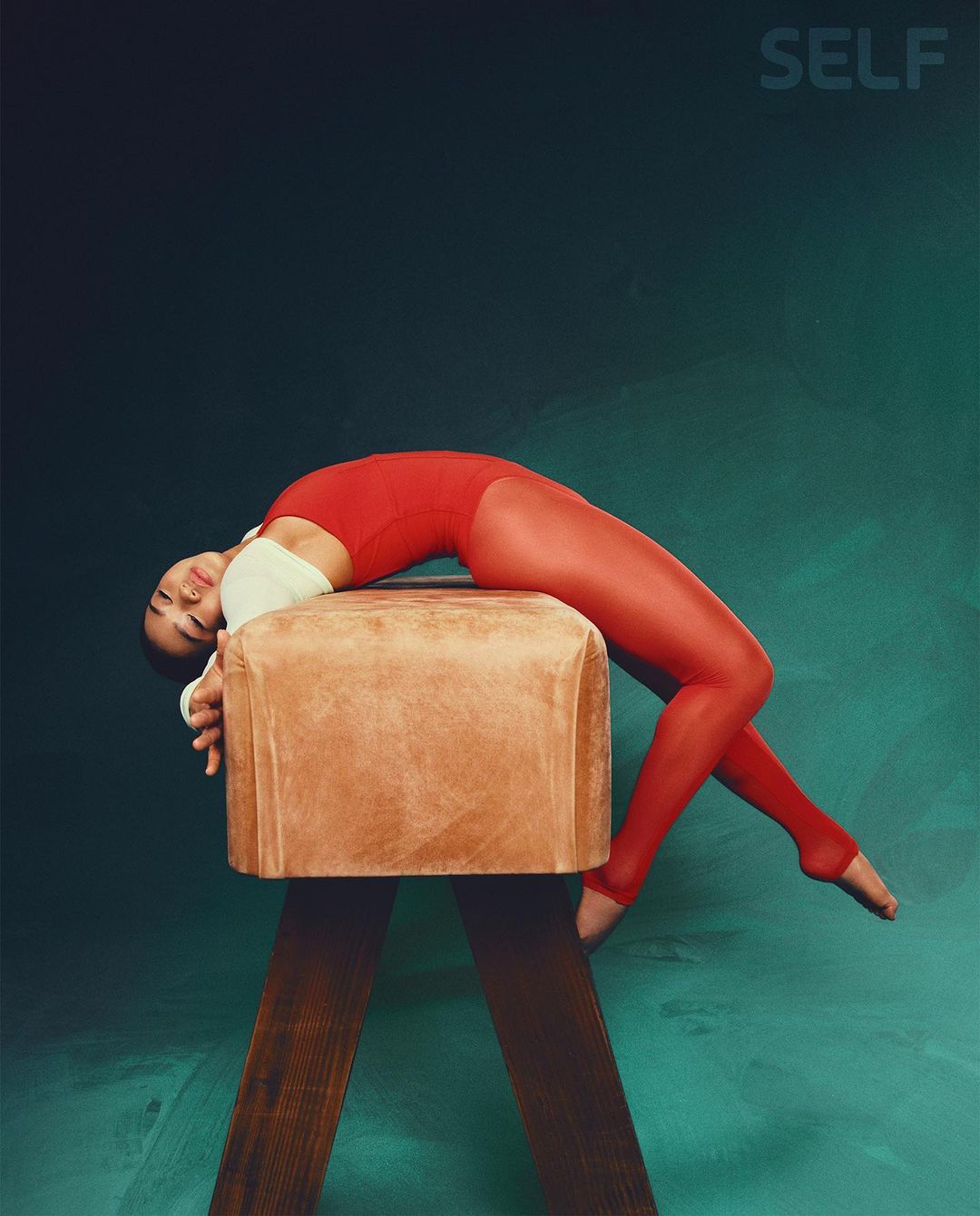 Gymnast in red leotard and tights arches back on a pommel horse against a teal and black background in a studio shot for a magazine.