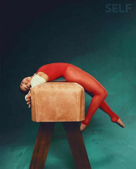 Gymnast in red leotard and tights arches back on a pommel horse against a teal and black background in a studio shot for a magazine.