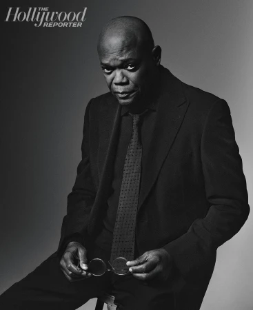 Portrait of Samuel L. Jackson in a dark suit and tie, seated and holding eyeglasses against a grey gradient backdrop, with The Hollywood Reporter logo.
