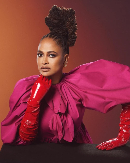 Glamorous studio portrait of a woman with an elaborate hairstyle and bright pink dress wearing long, shiny red gloves.