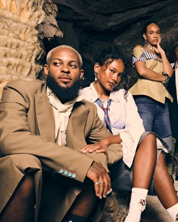 Group of four people sitting in a cave wearing stylish clothing and jewelry, posing for a portrait-style fashion shot.