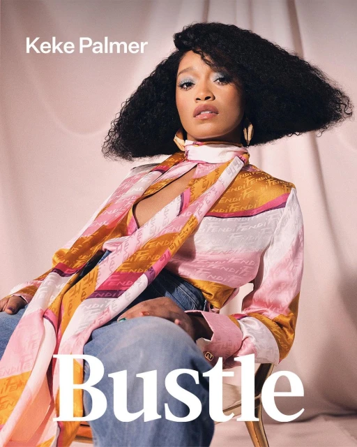 Keke Palmer poses for a portrait, wearing a Fendi scarf-blouse and blue jeans, against a light pink backdrop for Bustle magazine.