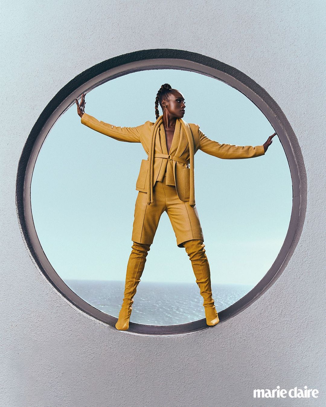 Fashion editorial shot of a Black woman posing in a yellow suit and matching boots inside of a round architectural structure.