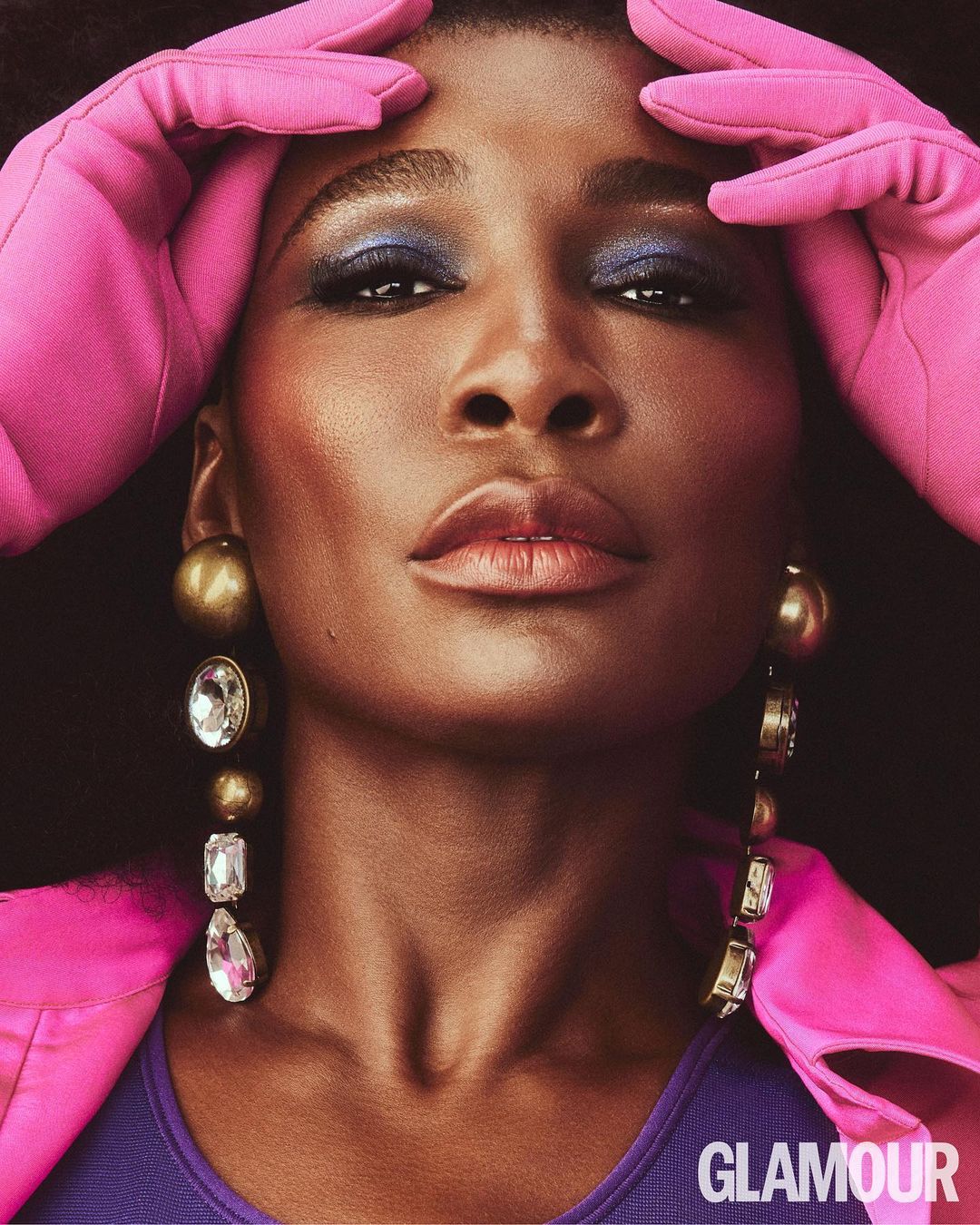 Close-up portrait of Venus Williams with pink gloves framing face, metallic eyeshadow, large earrings, shot for Glamour magazine.