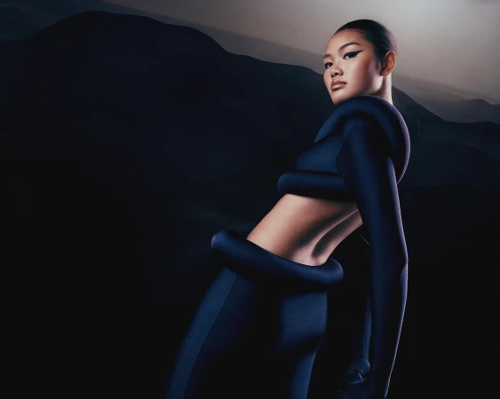 Glamour shot of Asian female model wearing stylish blue outfit against a mountain backdrop, showcasing fashion and scenic beauty.