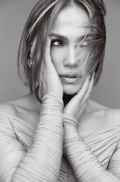 Jennifer Lopez portrait. Black and white headshot of the singer with her hands to her face, wearing an off-the-shoulder dress.