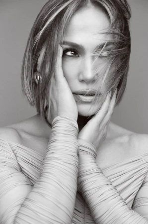Jennifer Lopez portrait. Black and white headshot of the singer with her hands to her face, wearing an off-the-shoulder dress.