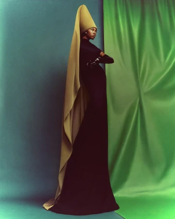 Model in long black dress and tall conical hat with drape, photographed by Chrisean Rose