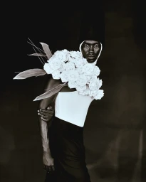 Portrait of a Black man wearing a tall dark headpiece and large white floral arrangement by Chrisean Rose