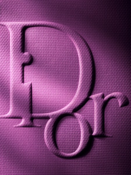 Close-up of the 'Dior' logo embossed on a pink, textured surface with studio lighting.