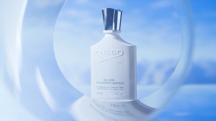 Creed Silver Mountain Water perfume bottle on a reflective surface with a blue and white background featuring transparent sphere shapes.