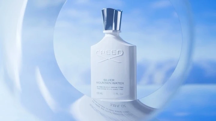 Creed Silver Mountain Water perfume bottle on a reflective surface with a blue and white background featuring transparent sphere shapes.