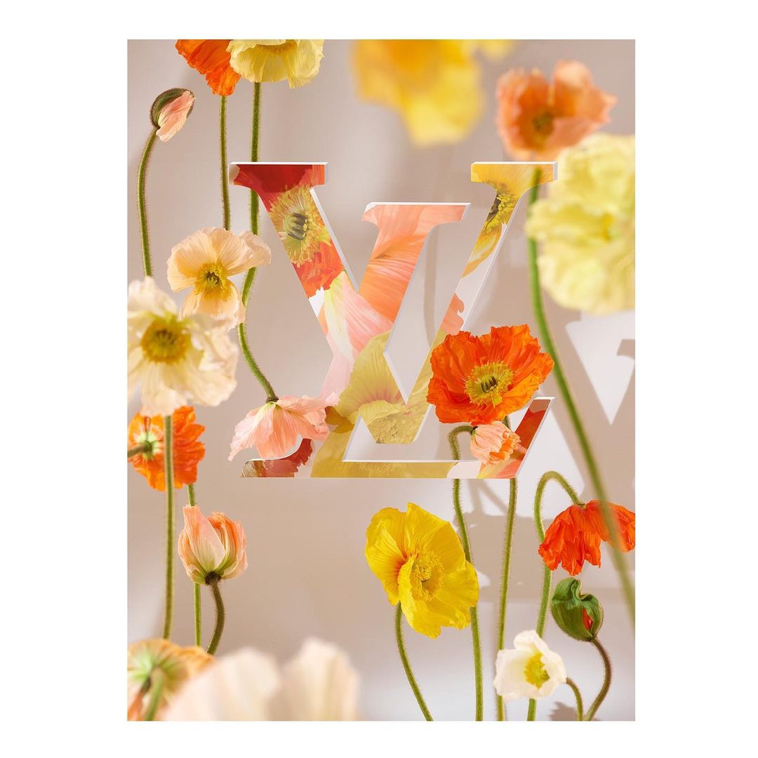 Stylized floral arrangement featuring orange and yellow poppies around a Louis Vuitton logo against a soft, neutral background.