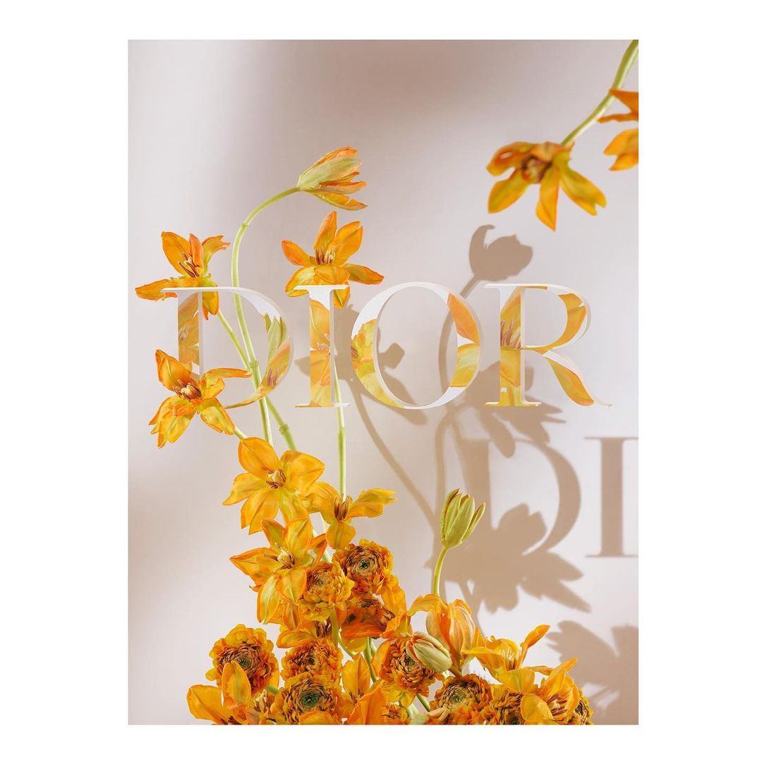 Floral still life of bright yellow orchids with cut-out DIOR text casting a shadow in a photo studio, high key lighting.