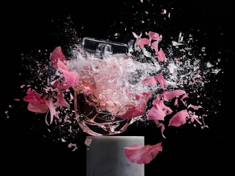 High-speed shot of a shattering perfume bottle surrounded by pink rose petals and glass shards against black