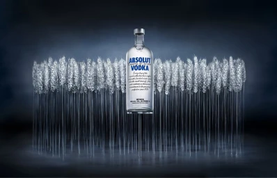 Absolut vodka bottle standing upright behind a horizontal row of frost-covered wheat stalks on a dark textured background