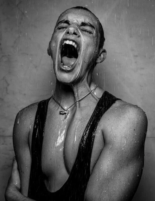 Dramatic black and white portrait of a young adult in a tank top, screaming with mouth open under water falling, with marble wall background.