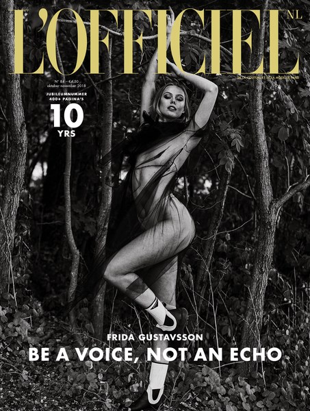 L'Officiel NL cover featuring model Frida Gustavsson in a sheer outfit, set against a grayscale woodland backdrop, with bold magazine typography.