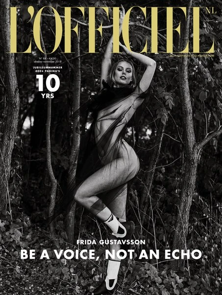 L'Officiel NL cover featuring model Frida Gustavsson in a sheer outfit, set against a grayscale woodland backdrop, with bold magazine typography.