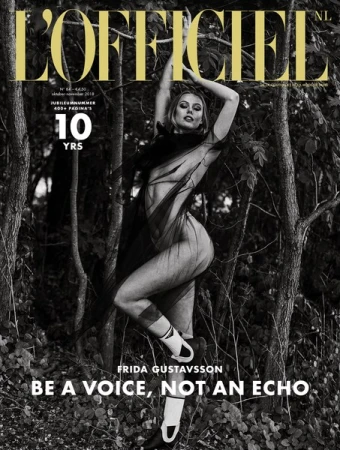 L'Officiel NL cover featuring model Frida Gustavsson in a sheer outfit, set against a grayscale woodland backdrop, with bold magazine typography.