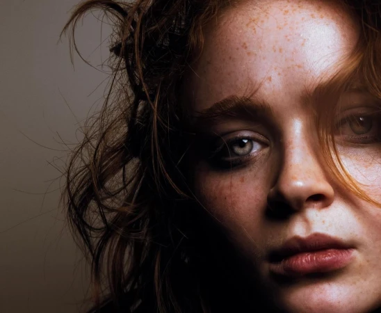 Close-up portrait of a woman with red hair and prominent freckles against a neutral background by photographer Damon Baker.