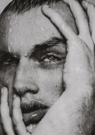 Close-up monochrome portrait of a man with wet hair and water droplets on his face, holding his head with both hands.