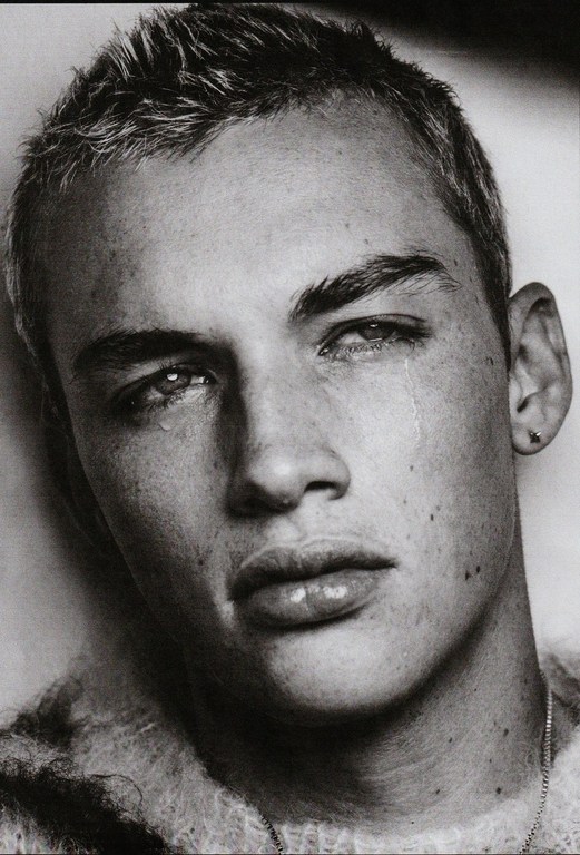 Striking black and white portrait of a young adult male with short hair and a slight frown, complete with visible water droplets suggesting tears.