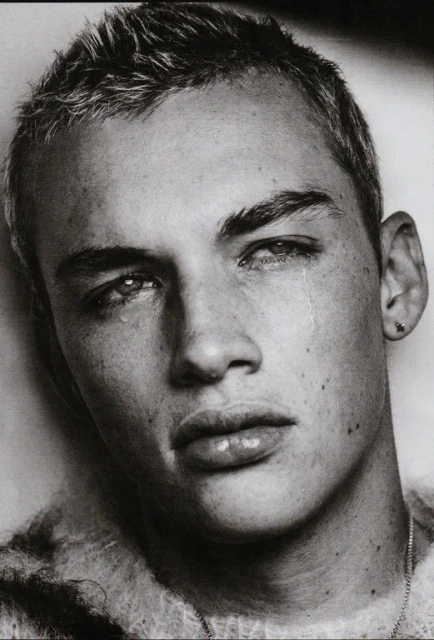 Striking black and white portrait of a young adult male with short hair and a slight frown, complete with visible water droplets suggesting tears.