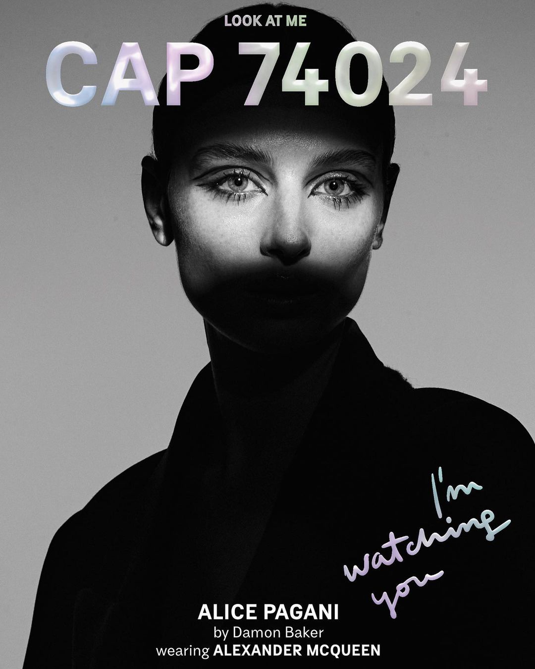 Monochrome portrait of a woman with stylized makeup and short hair, wearing a dark garment with text overlay, 'I'm watching you'.