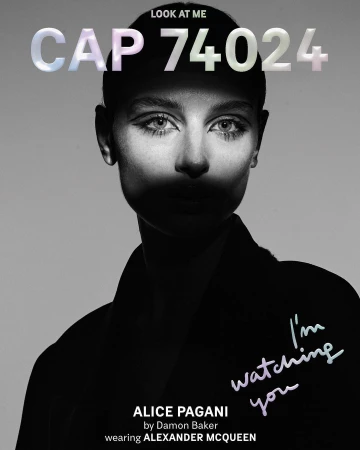 Monochrome portrait of a woman with stylized makeup and short hair, wearing a dark garment with text overlay, 'I'm watching you'.