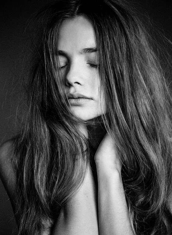 Close-up black and white portrait of a young woman with long dark hair covering her face and eyes closed.