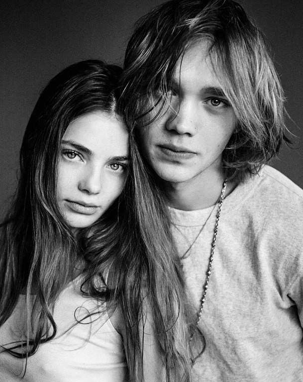 Black and white portrait of a young adult couple. The woman and man are close together, looking at the camera in a photo studio.