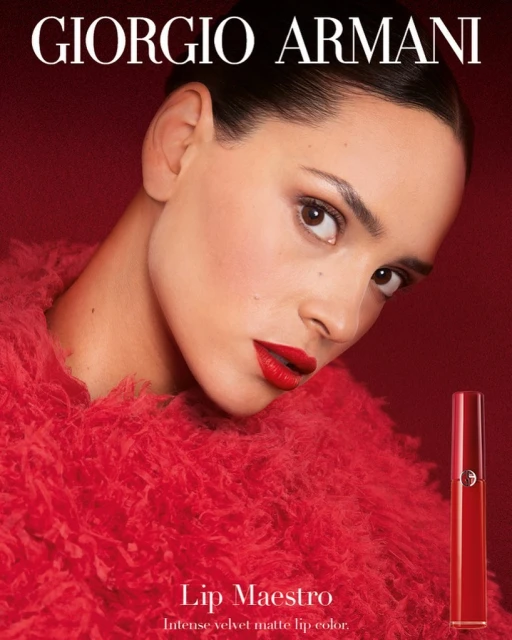 Close-up beauty shot of a woman with red lipstick, wearing a furry red top against a matching background, with a lipstick tube prop.