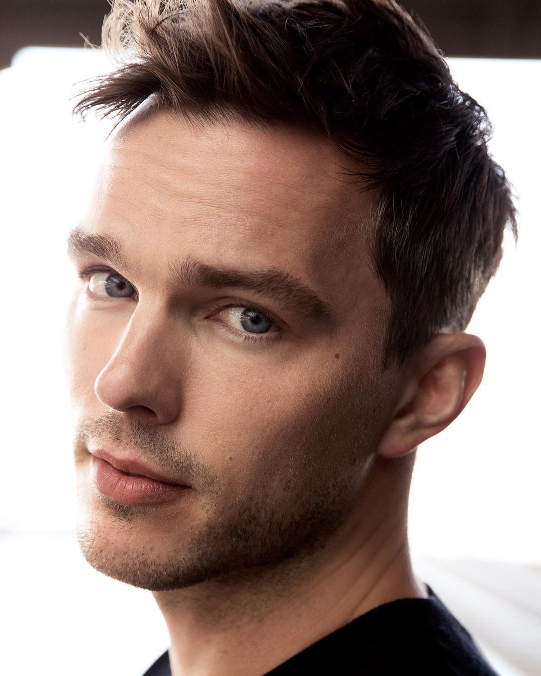 Close-up portrait of a light-skinned adult male with short dark hair, blue eyes, and a neutral expression, wearing a dark shirt.