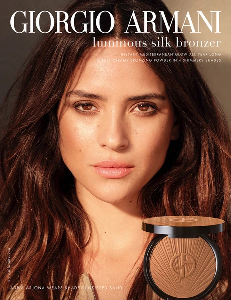 Beauty shot of a woman with dark brown hair wearing makeup, posing in front of a bronzer compact and Giorgio Armani ad copy.