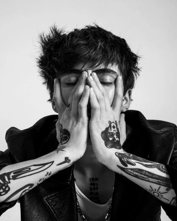 Monochrome portrait of a tattooed man holding his hands to his face against a plain light background