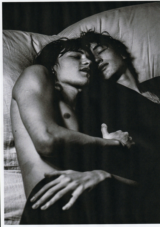 Two young men lying close together asleep in bed, captured in a monochrome photographic portrait by Damon Baker.