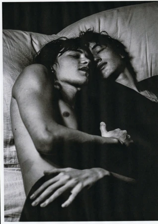 Two young men lying close together asleep in bed, captured in a monochrome photographic portrait by Damon Baker.