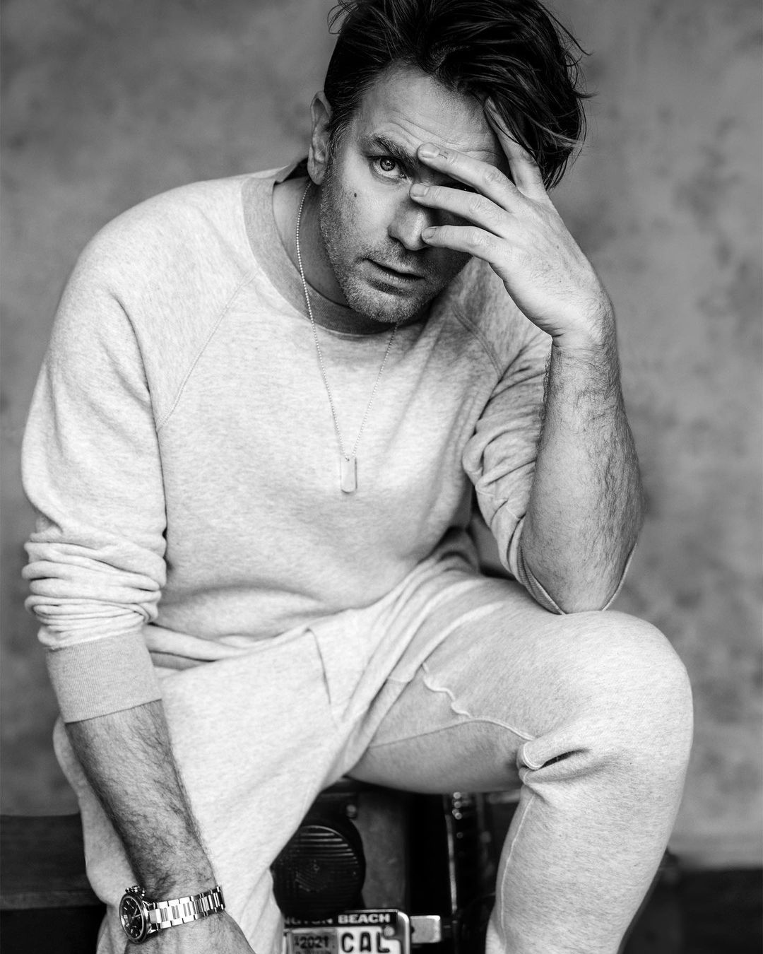 Black-and-white portrait of a fair-skinned adult male model with hand on his face, wearing a sweatshirt and metal watch.