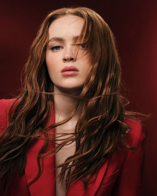 Close-up studio portrait of a young adult female with red hair wearing a red jacket against a red background, beauty and fashion.