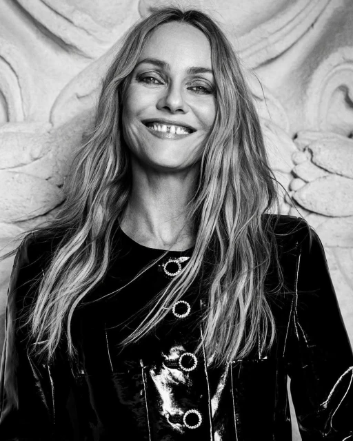 Monochrome portrait of a smiling woman with long hair wearing a patent-leather jacket against a textured background. Fashion and beauty.