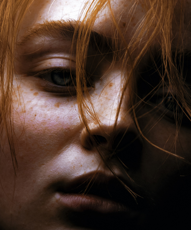 Close-up portrait of a woman with red hair and freckles falling across her face by Damon Baker